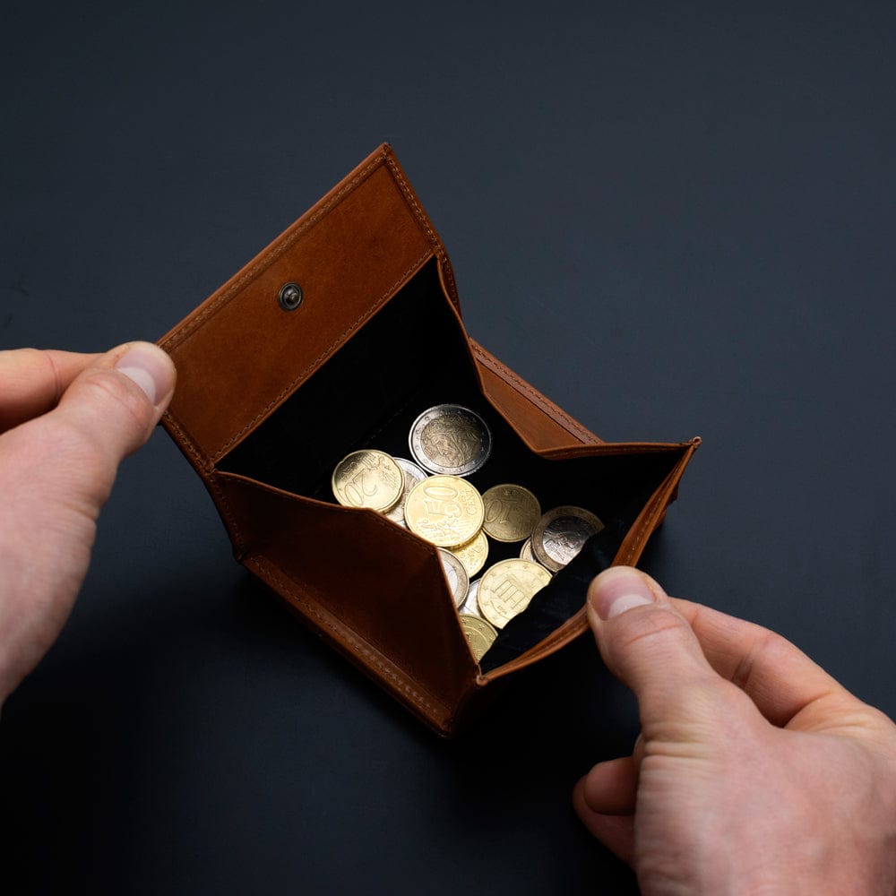 Brown leather magic wallet from jaimie jacobs with coins held by hands against a dark background