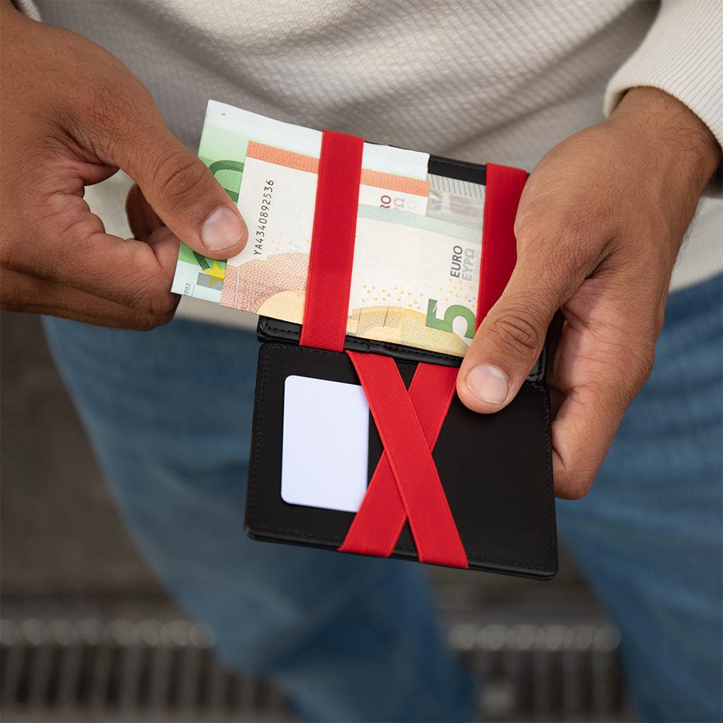 Person holding a black magic wallet with red rubber bands and is pulling out money, blurred background