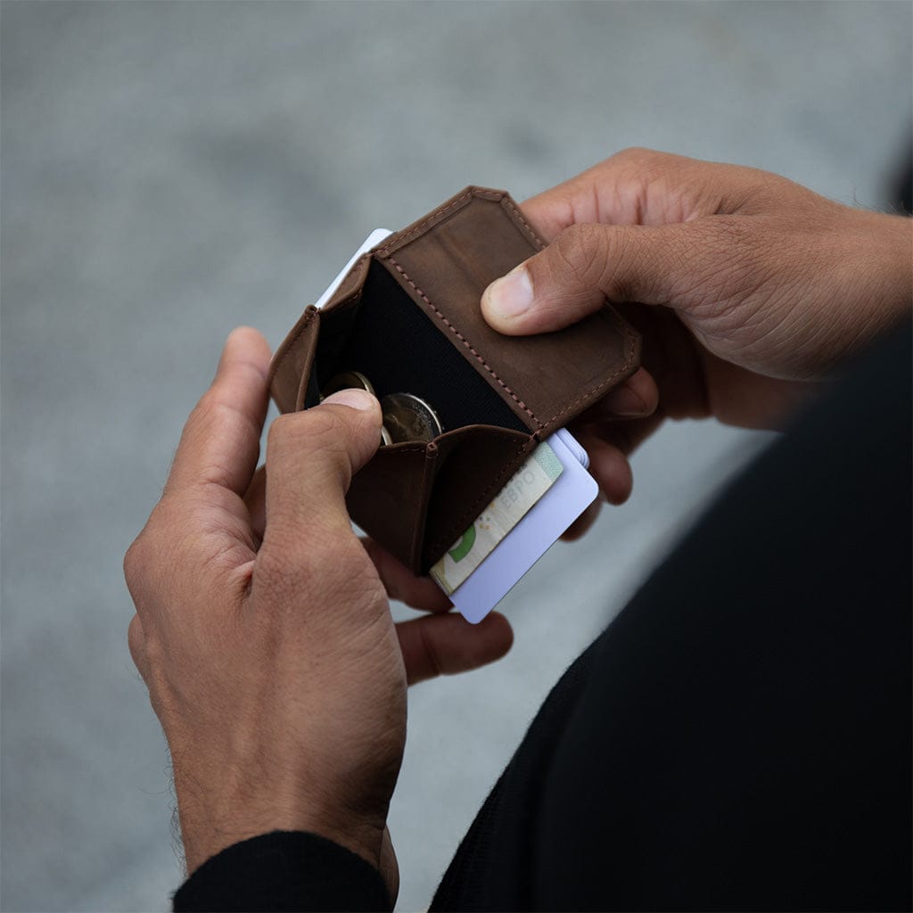 Person opening a brown nano boy pocket leather wallet with coins and cards on a blurred background