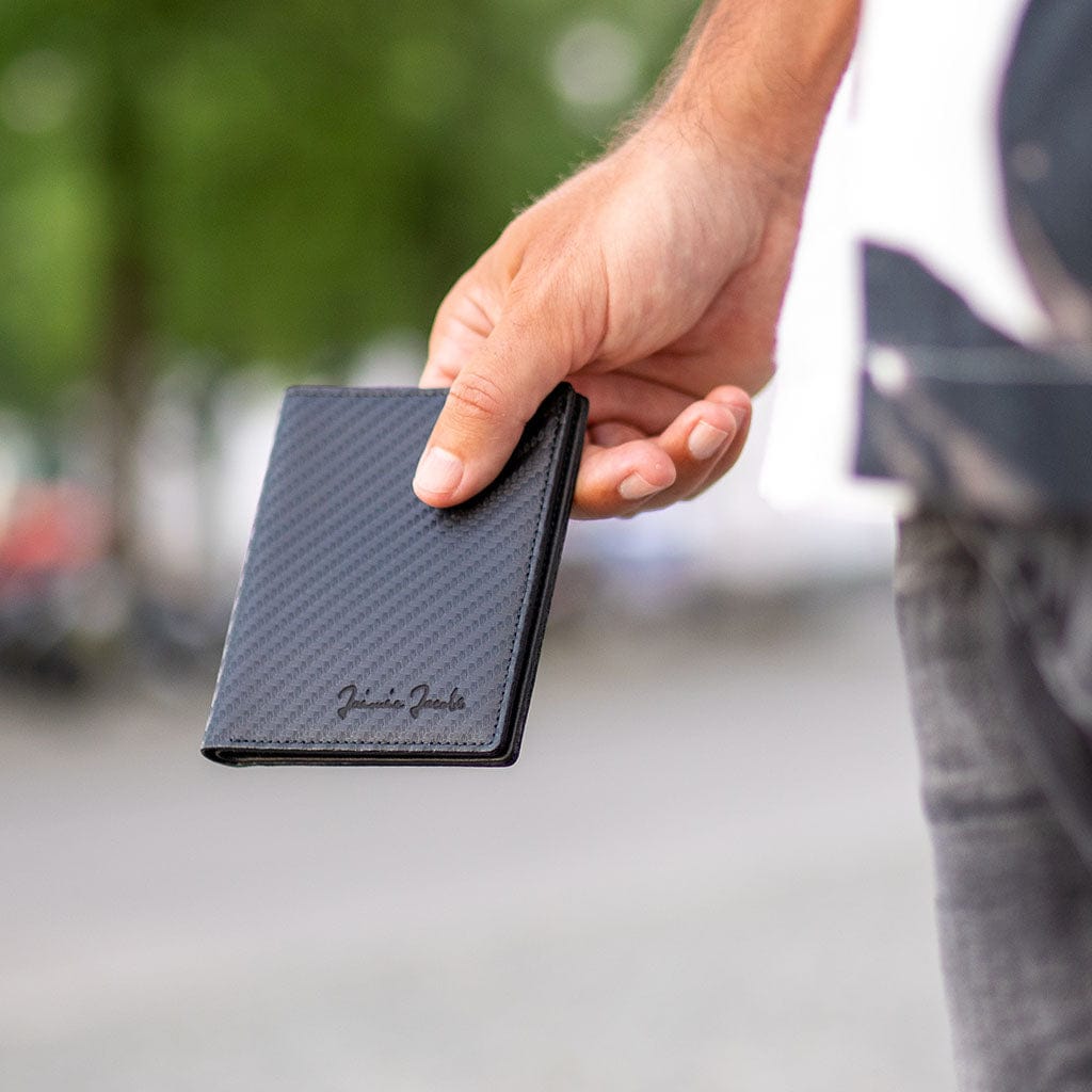 Hand holding a black slimstar wallet with jaimie jacobs branding outdoors.